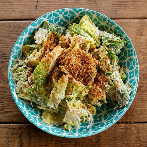 Caesar salad with romaine lettuce, creamy dressing, and crispy breadcrumbs in a patterned blue bowl.