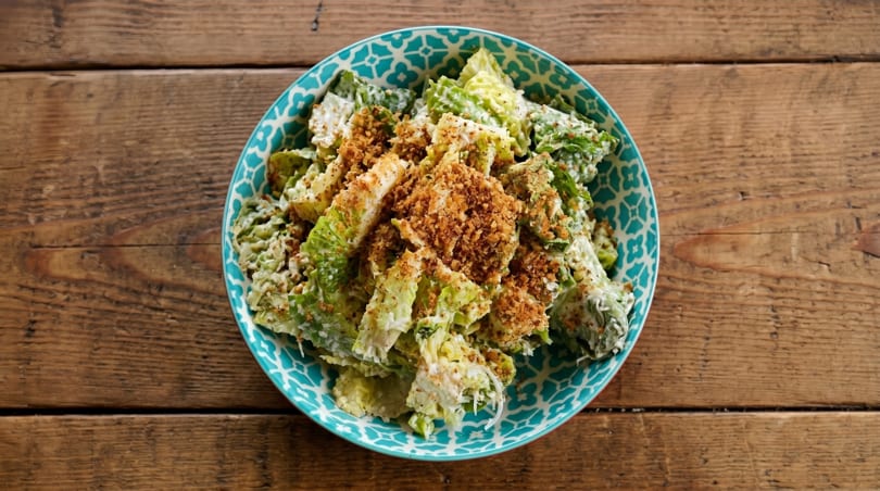 Caesar salad with romaine lettuce, creamy dressing, and crispy breadcrumbs in a patterned blue bowl.